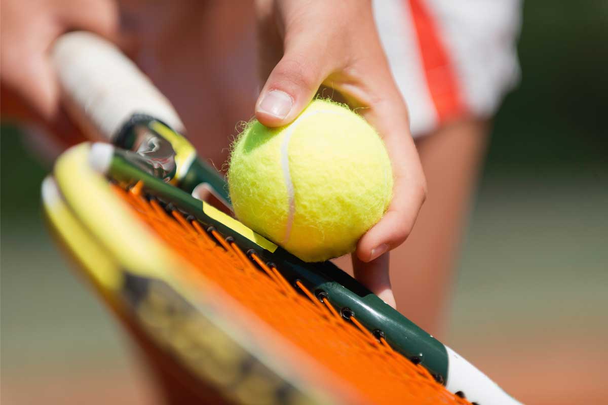 Close-up of a person holding a tennis racket and a bright yellow tennis ball, ready for an adventure on the court. The orange strings add a vibrant touch, reminiscent of Maui's sunsets. The background fades into a blur, highlighting the moment's energy and focus.